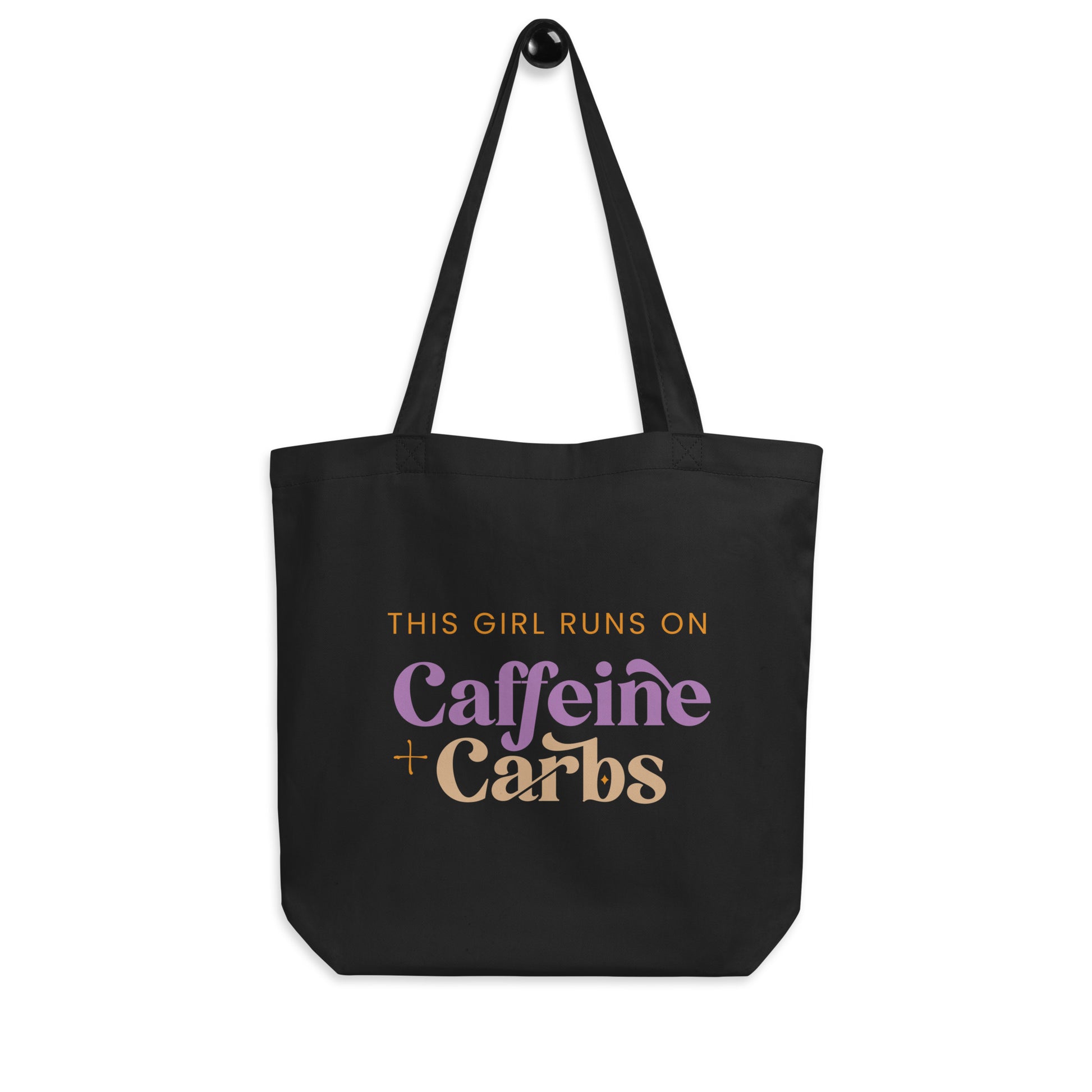 black cotton tote bag that says "This girl runs on caffeine + carbs"