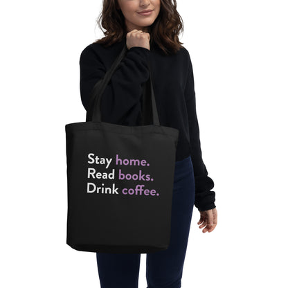 Woman holding black tote bag that says Stay home, read books, drink coffee