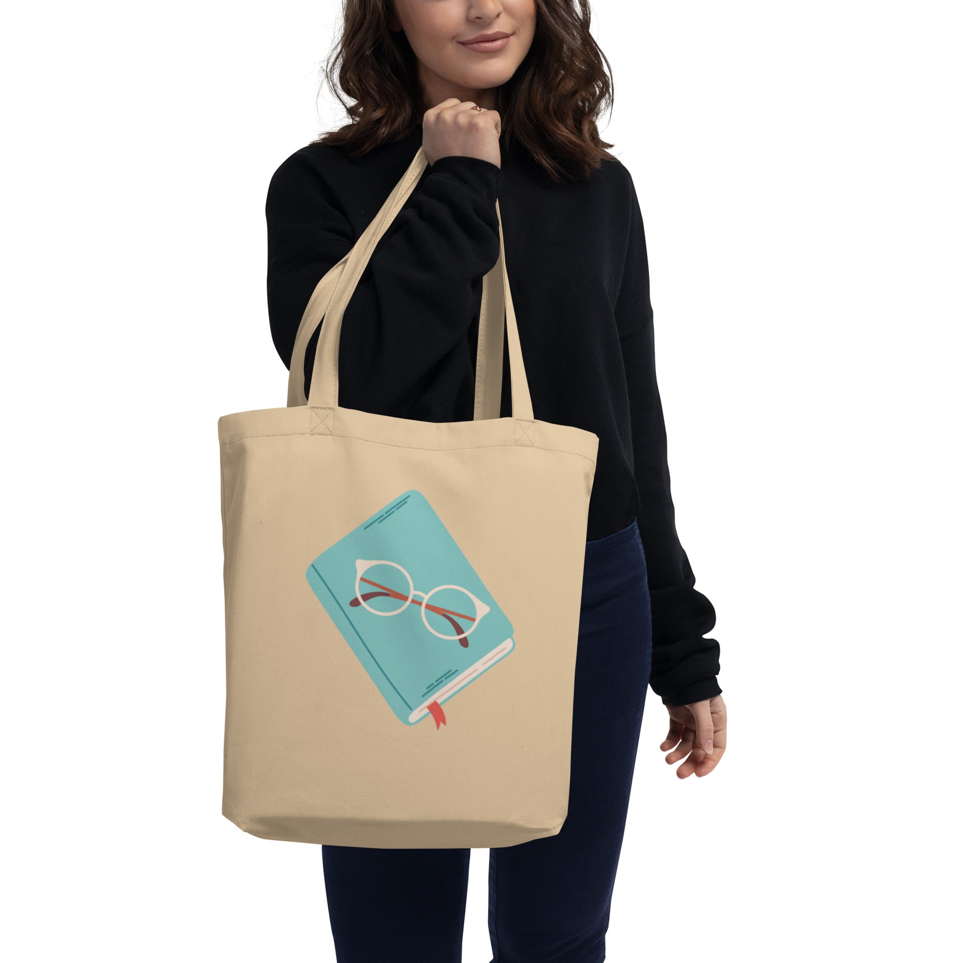 Woman hold tan canvas cotton tote bag with a cute illustration of a teal book with glasses on top